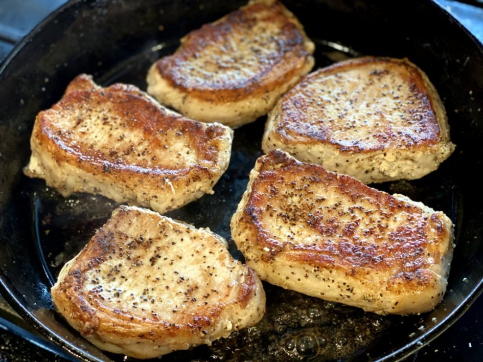 Pan searing pork chops in a cast iron skillet. 