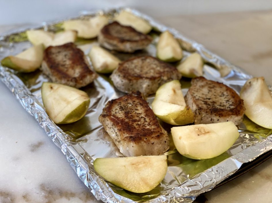 Seared pork chops and pears placed on a baking pan to go into the oven.