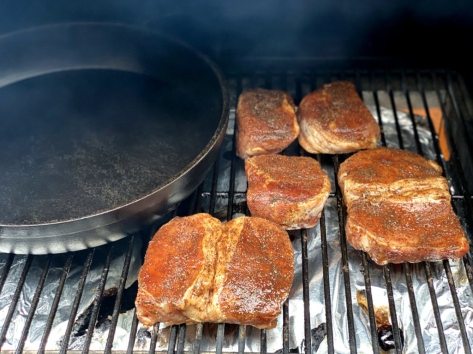 Seasoned pork chops and a black cast-iron skillet on the grill.