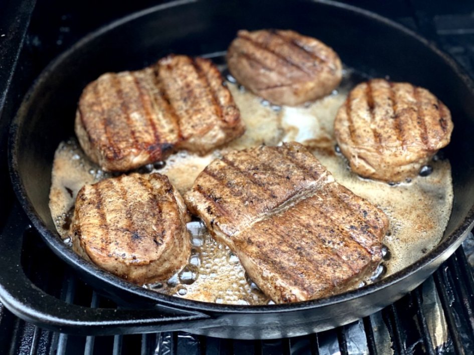 Pork chops with grill marks place in a cast-iron skillet with melted butter. 