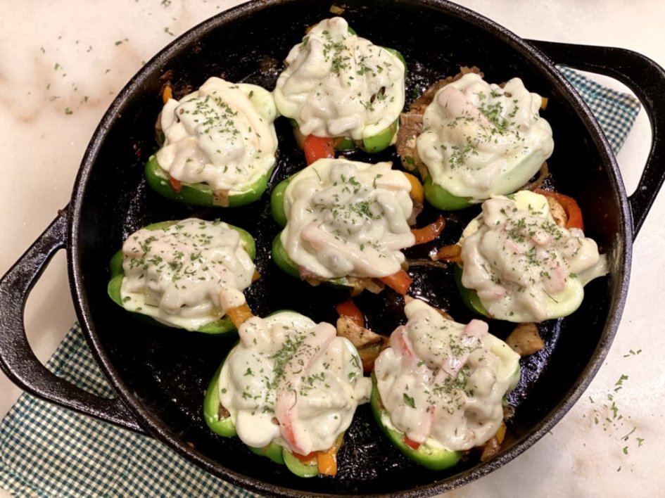 Baked Cheesesteak Stuffed Peppers with melted cheese and sprinkled with dried parsley in a castiron skillet.