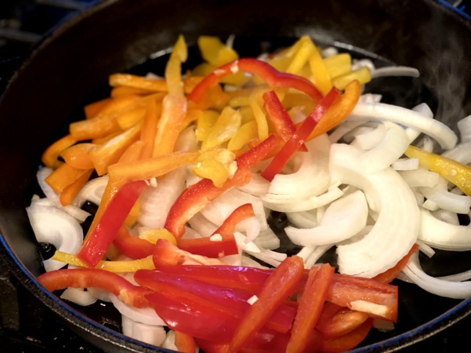 Colorful strips of peppers and onions in a cast-iron skillet