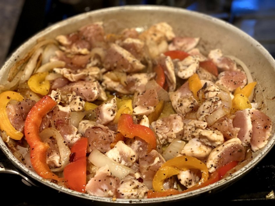 Chicken, onions and peppers in a skillet.