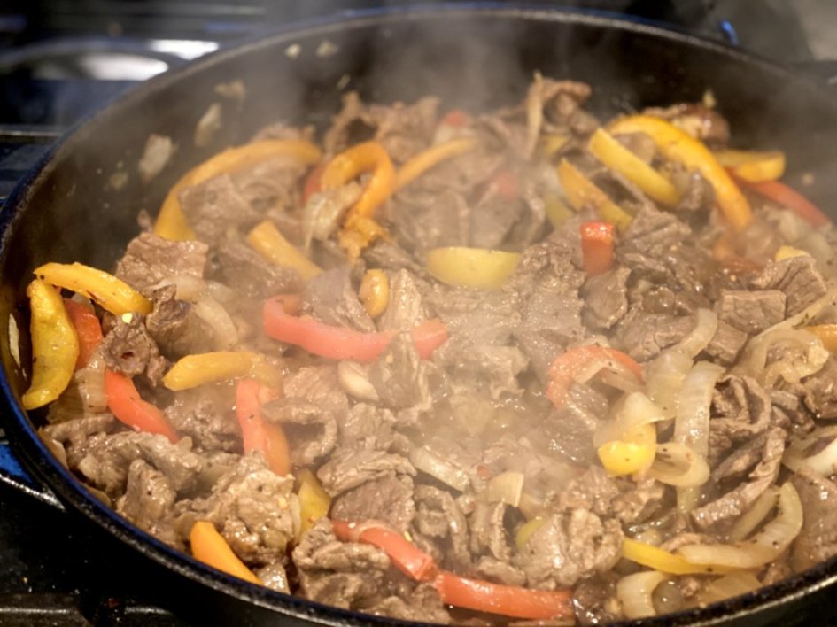 Steak is cooking in the skillet with the onions and peppers. 
