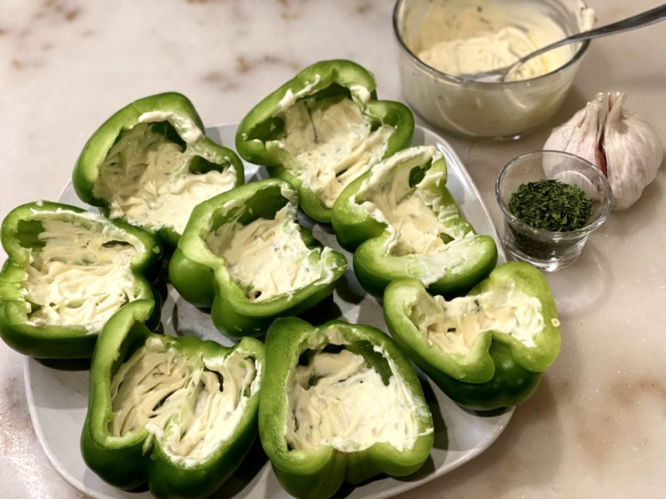 Spoonful of garlic aioli sauce is dropping into the bottom of each halved bell pepper. 