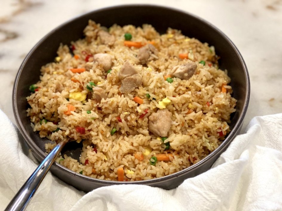 Fried rice full of veggies, chicken, and eggs in a large bowl with a silver fork and white napkin. 