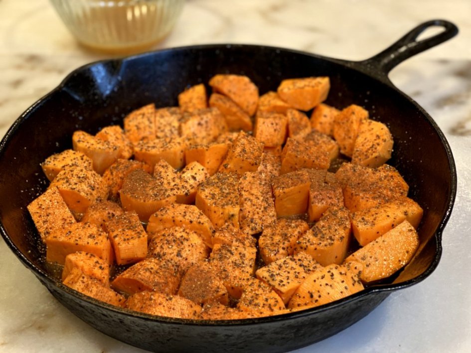 chopped sweet potatoes seasoned and placed in a black cast-iron skillet. 