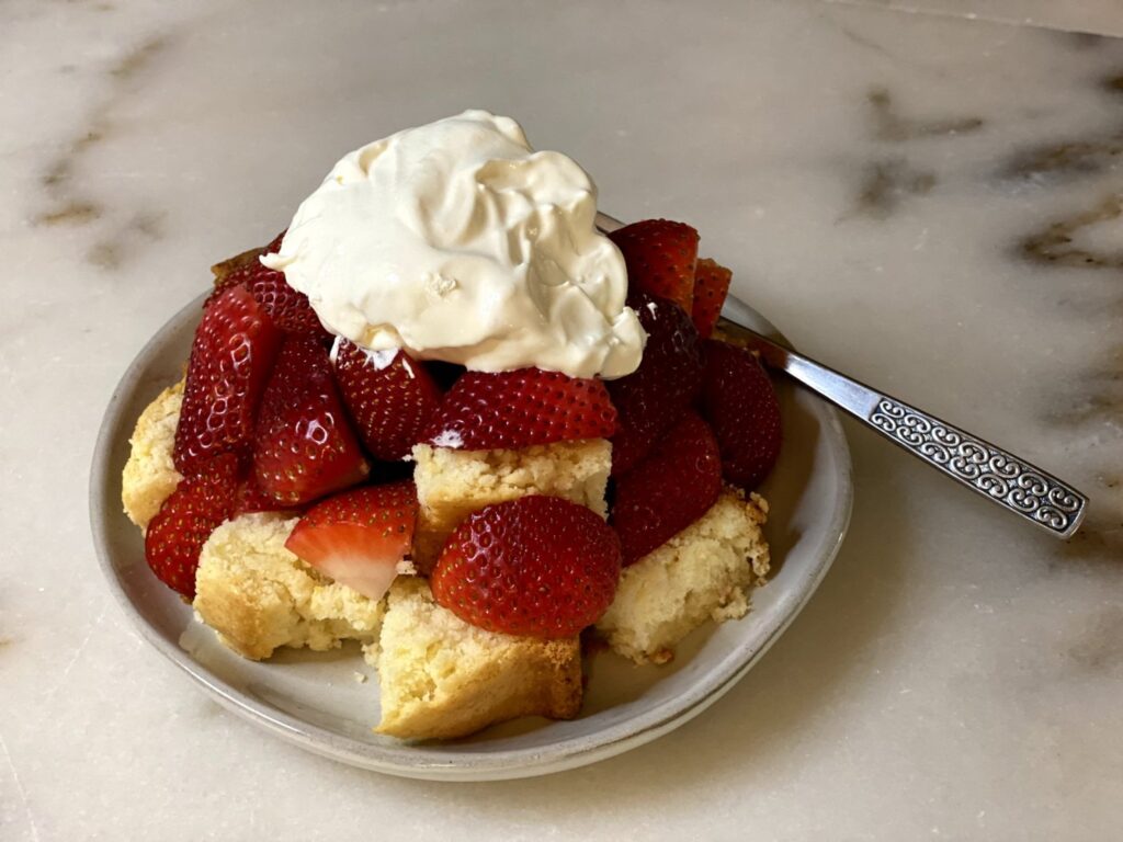 easy lemon pound cake recipe cut into bite-sized squares topped with freshly cut strawberries and homemade whipped cream. 