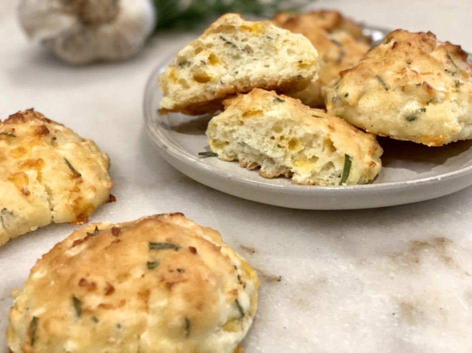 Rosemary cheddar drop biscuits with garlic butter on a plate with garlic and rosemary in the background.
