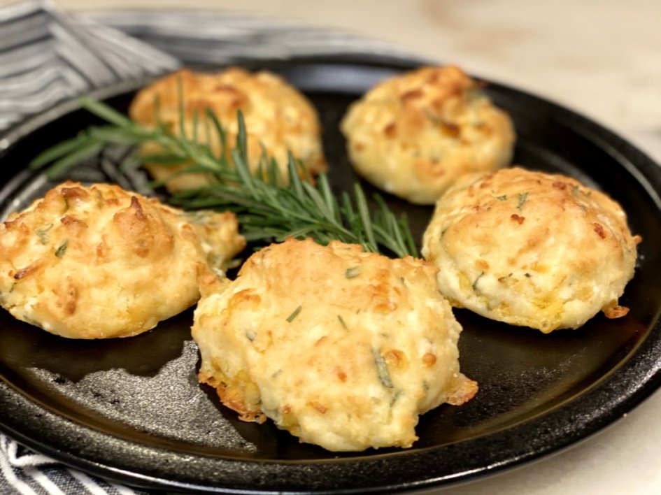 cheddar drop biscuits on a black plate with sprigs of rosemary.