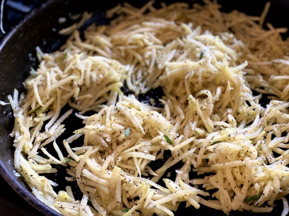 Cooking shredded potatoes and herbs in a cast iron skillet