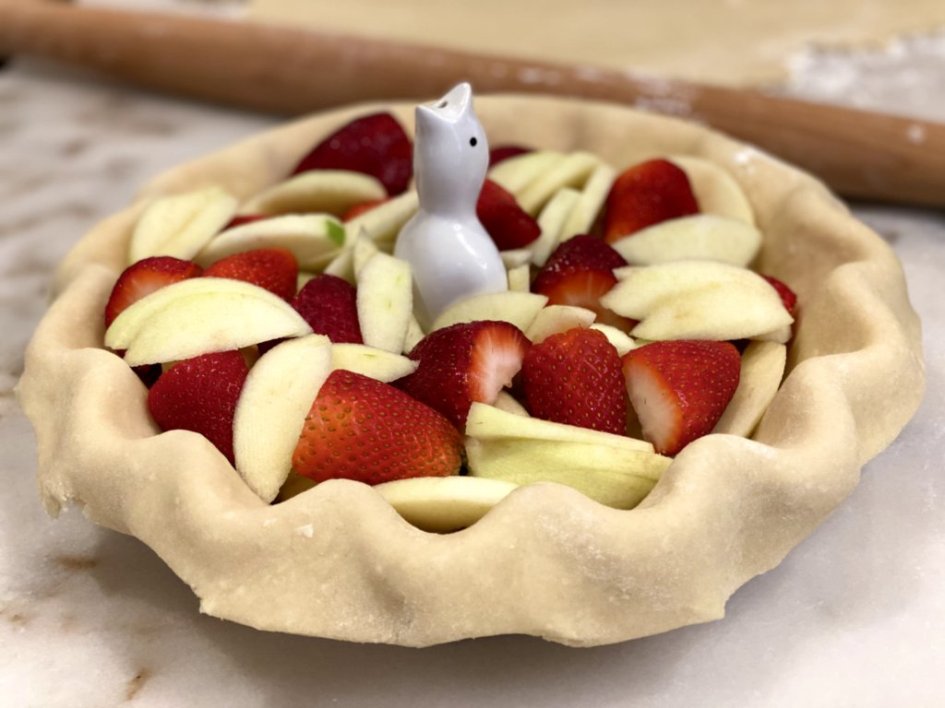 pie crust with freshly cut granny smith apples and sliced strawberries with a ceramic pie bird in the middle. 