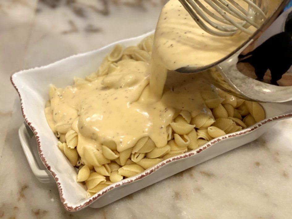 Pouring cheese sauce over the macaroni shells. 