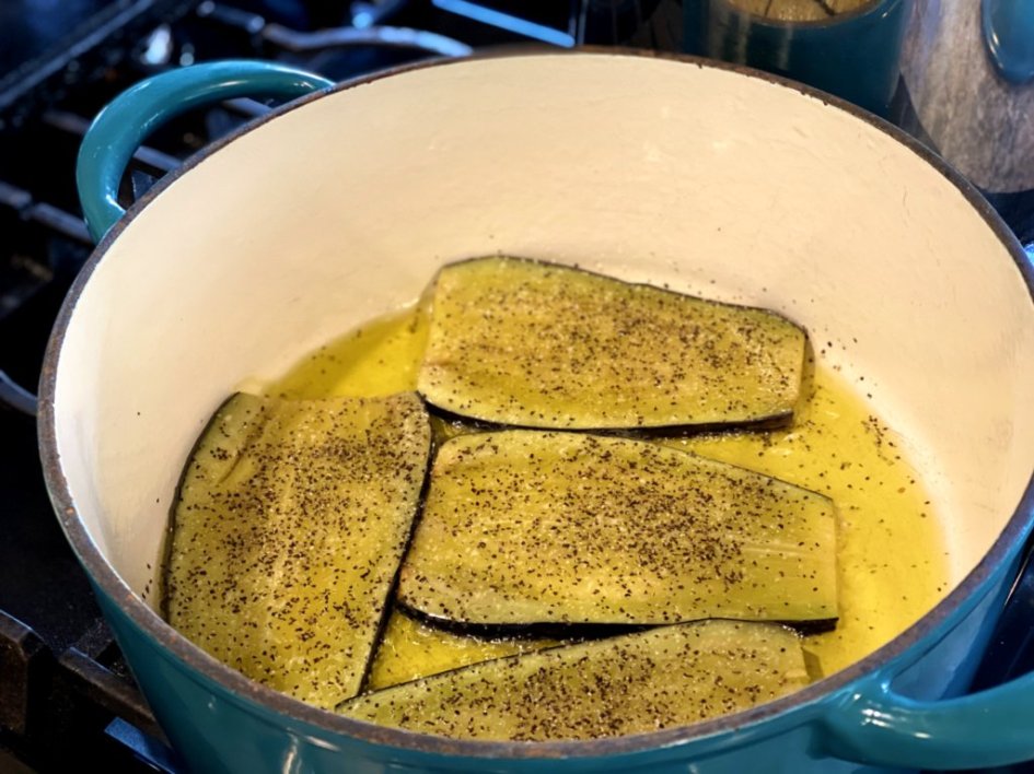 Browning slices of eggplant in olive oil in a blue cast iron dutch oven. 