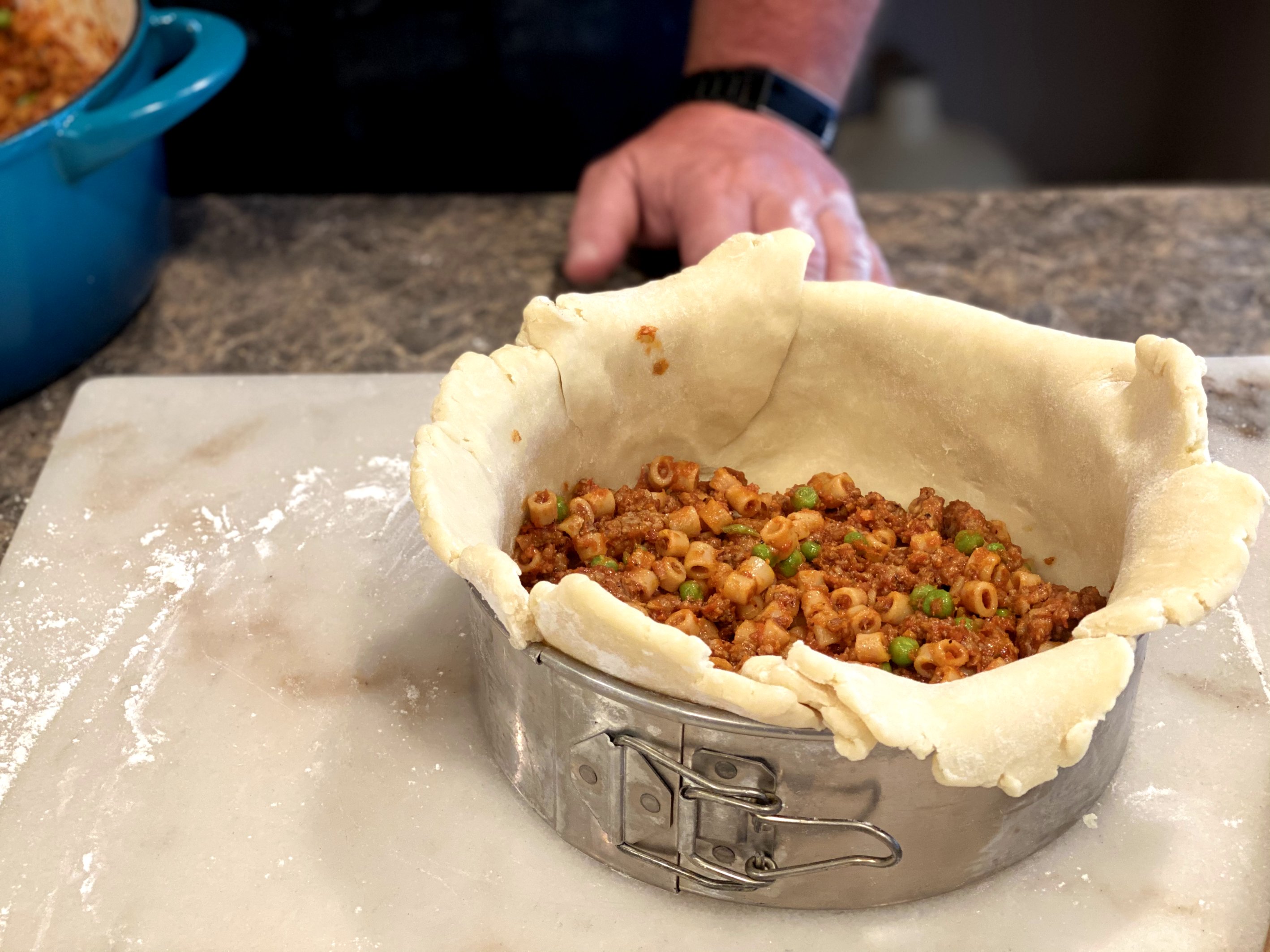 Filling the pie pastry with cooked pasta, peas, and meat sauce.