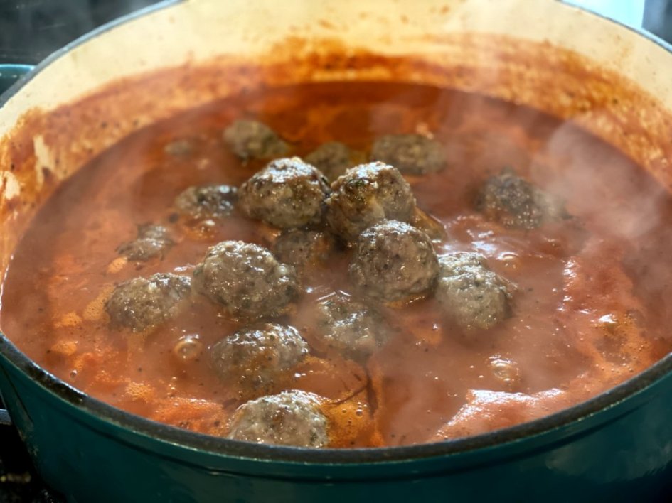 homemade pasta sauce is boiling in a Dutch oven with homemade meatballs simmering in the pot. 