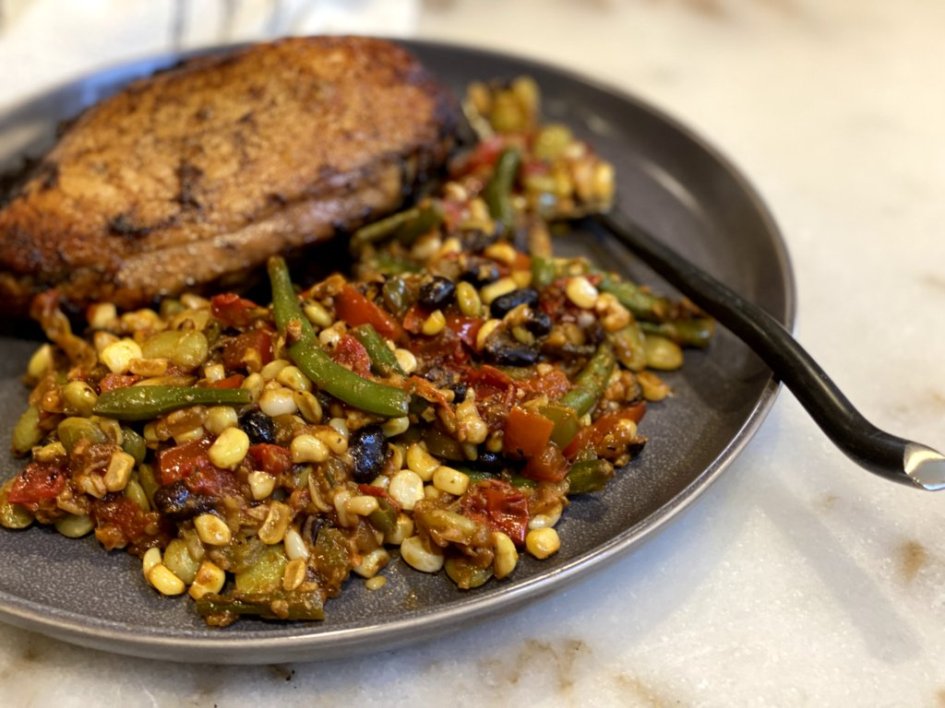 A plate full of succotash and seasoned grilled chicken breast. 