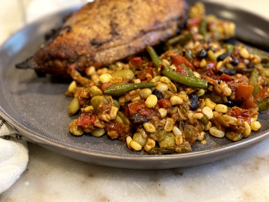 A gray stone plate filled with garden fresh succotash served with grilled chicken breast.