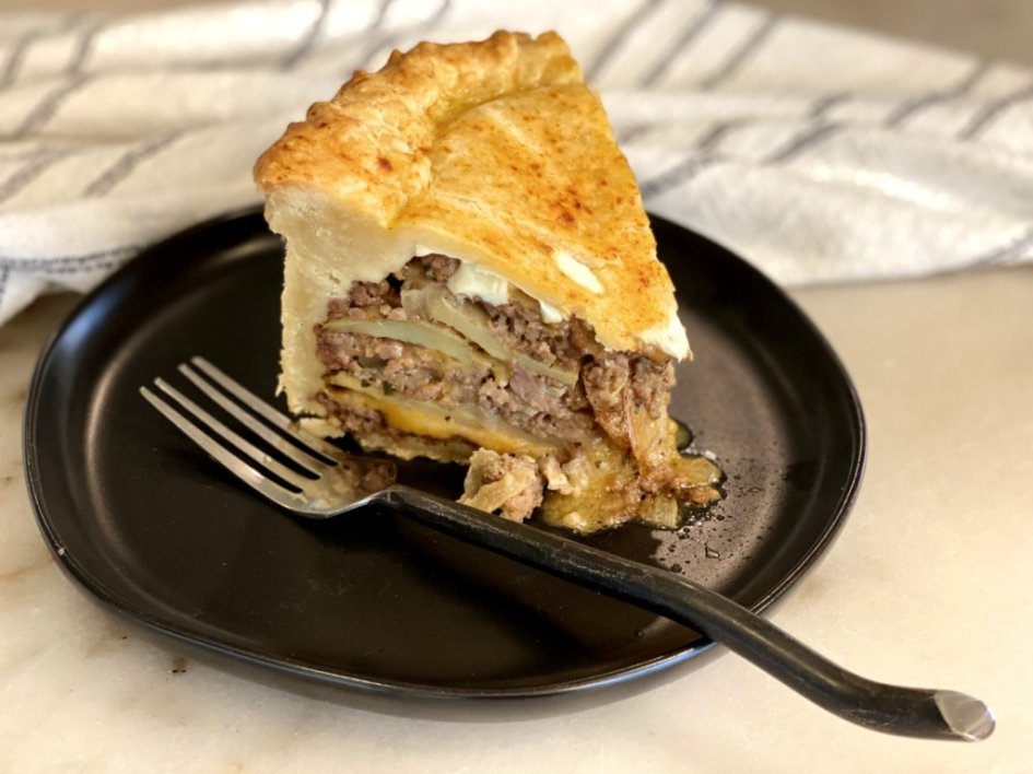 One large slice of meat and potato timballo pie on a black plate - ready to serve. 