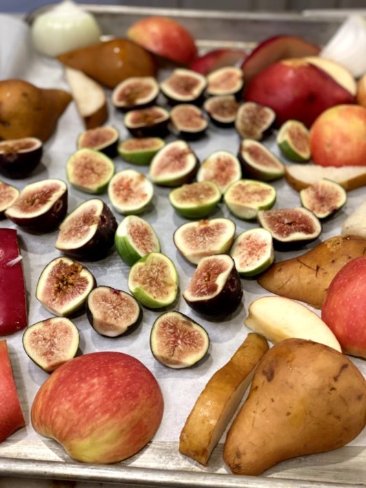 colorful cut pears, apples, onions, and figs on a baking sheet with parchment paper reading for roasting. 