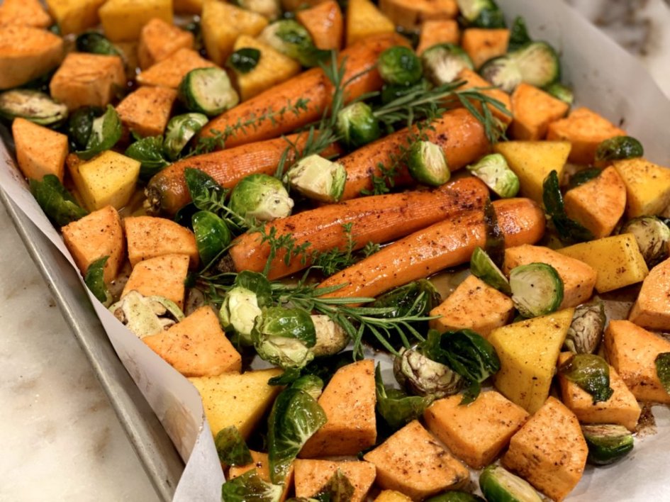 fresh butternut squash, sweet potatoes, carrots, brussels sprouts and herbs ready to roast in the oven on a sheet pan. 