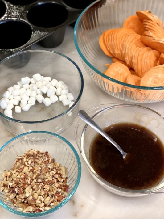 Slices of sweet potatoes covered in cinnamon with mixed nuts and marshmallows in the background. 