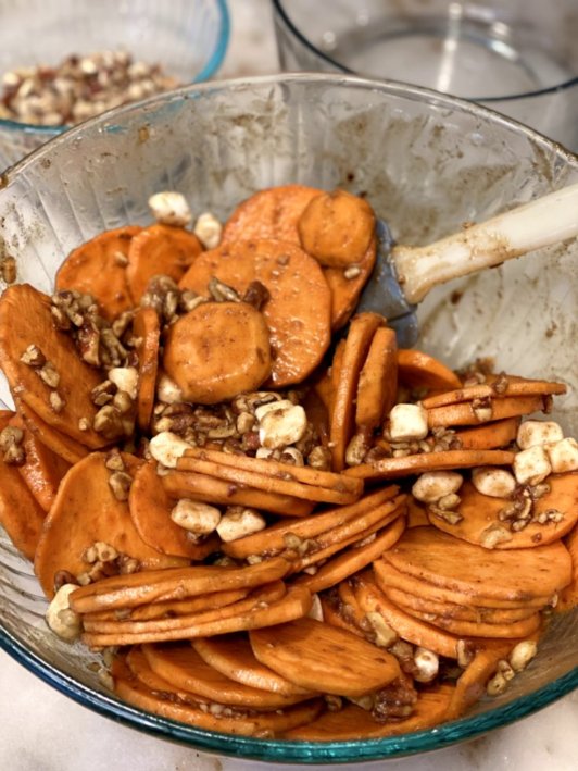 Mixing togeth the orange sweet potatoe slices with the chopped nuts and marshmallows, butter, brown sugar, and spices. 