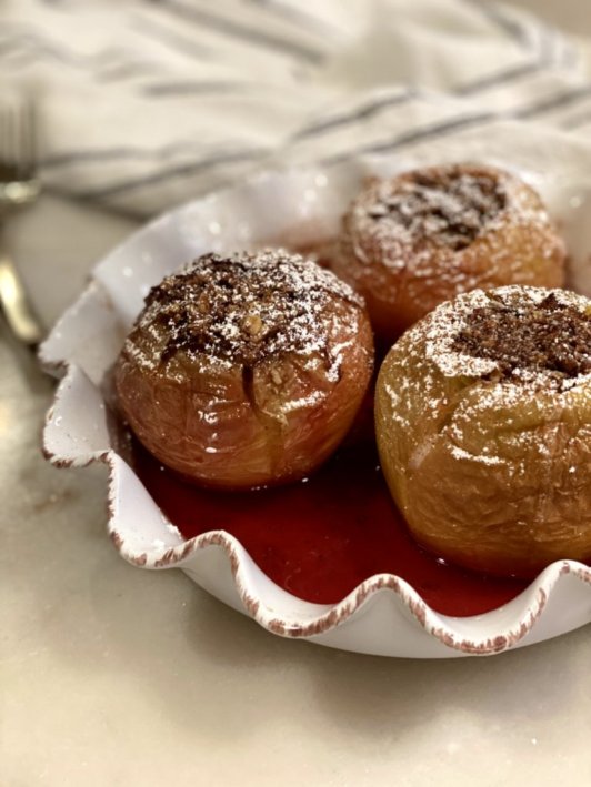 Pumpkin Spice Baked Apples topped with powdered sugar sitting in apple cider. 