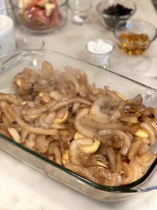 Sliced potatoes covered by sauteed onions in a glass baking dish. 