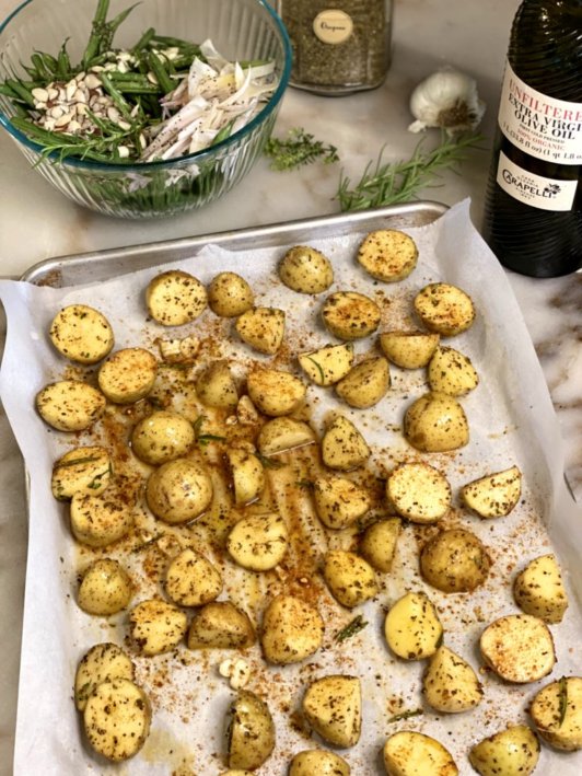 chopped baby gold potatoes on a baking sheet seasoned and sprinked with herbs