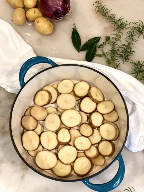 sliced potatoes in the bottom of a dutch oven pot. 