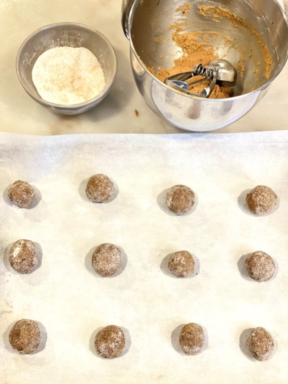 molasses cookie dough balls rolled in sugar and placed on a baking pan ready to go in the oven. 